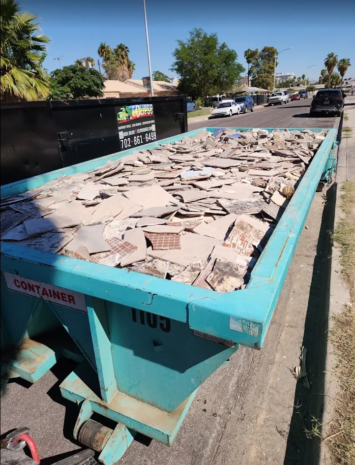 Blue dumpster filled with broken tiles on a residential street.