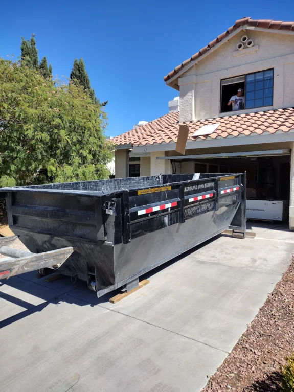 Large black Eclipse Waste dumpster in driveway while worker removes debris from second-story window.