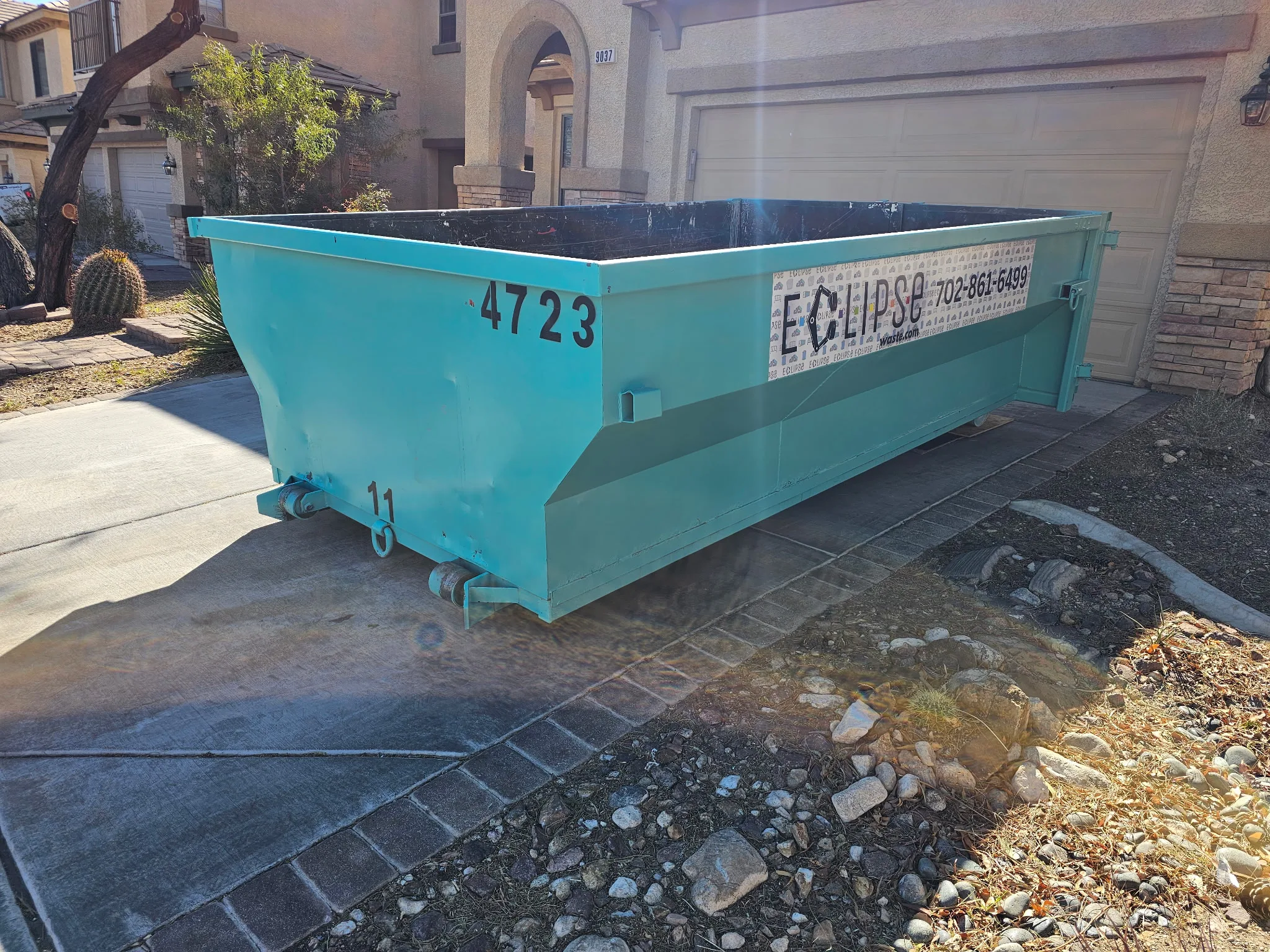 Teal Eclipse dumpster placed on a residential driveway in front of a garage
