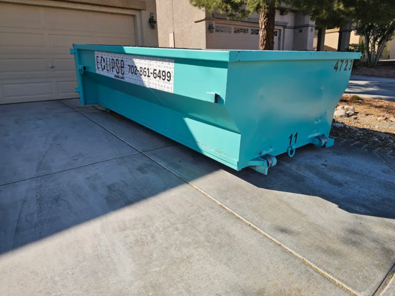 A large turquoise dumpster with the Eclipse logo placed in a residential driveway.